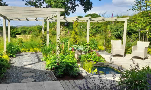 A landscaped garden with seating area, ponds, pergolas and planted beds in a new-build garden